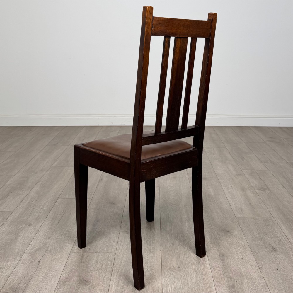Dark oak trestle dining table paired with six matching carved oak chairs with dark leather seats. View V