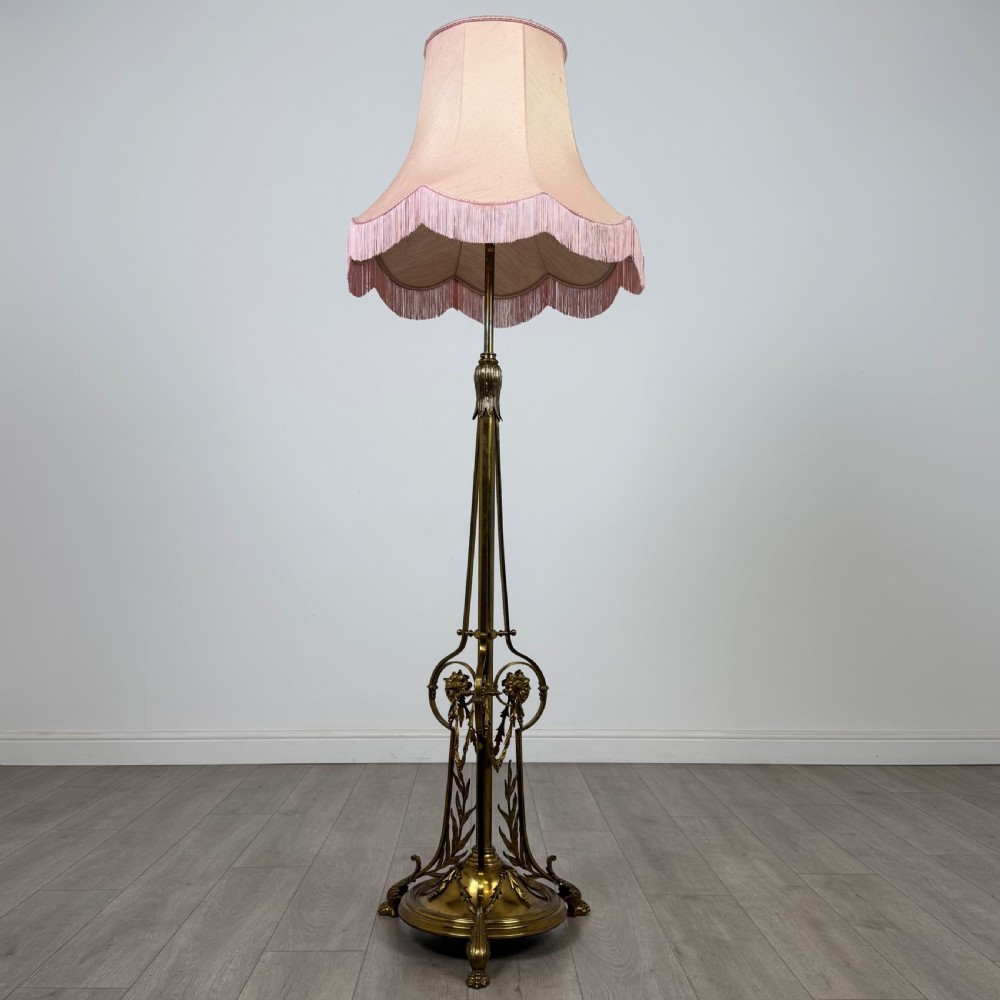 An antique 19th-century brass floor standing lamp featuring an ornate cast base with claw feet and a pink fringed shade. View II