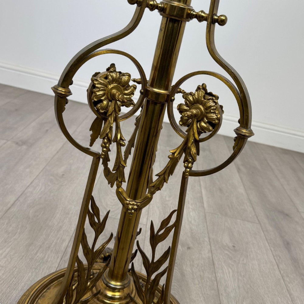 An antique 19th-century brass floor standing lamp featuring an ornate cast base with claw feet and a pink fringed shade. View X