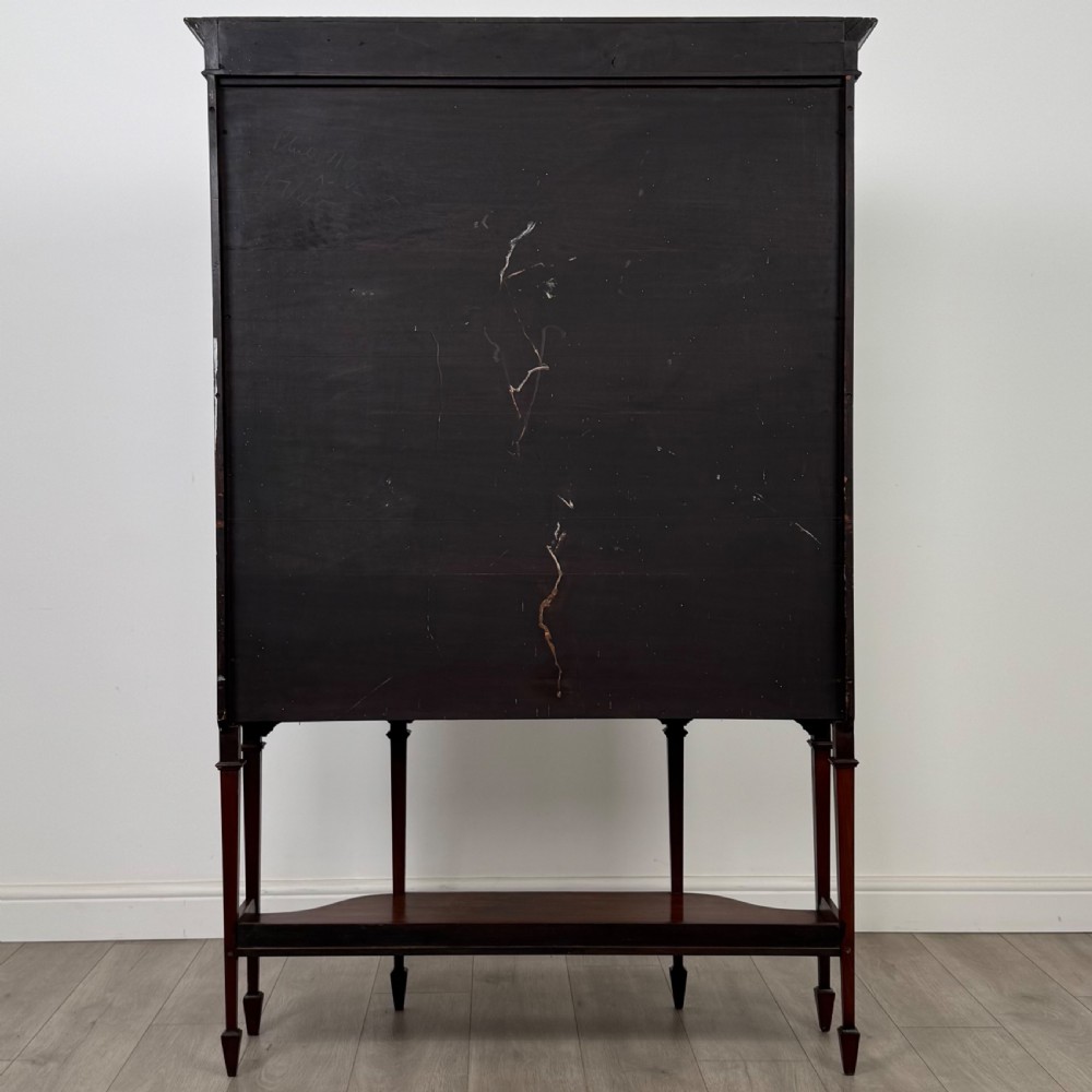 An Edwardian mahogany display cabinet featuring curved glass side panels, a glazed front door, fabric-lined interior shelves, and tapered square legs with a lower undertier. View VI