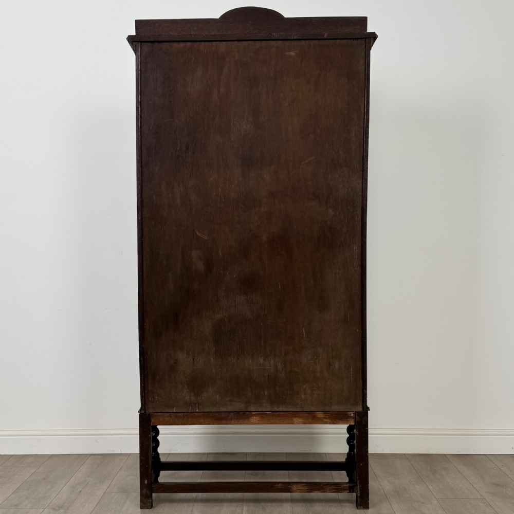 A dark oak Edwardian glazed display cabinet featuring two leaded glass doors, a lower drawer, and barley twist legs connected by stretchers. View VII