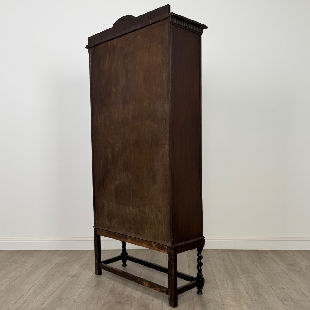 A dark oak Edwardian glazed display cabinet featuring two leaded glass doors, a lower drawer, and barley twist legs connected by stretchers. View X