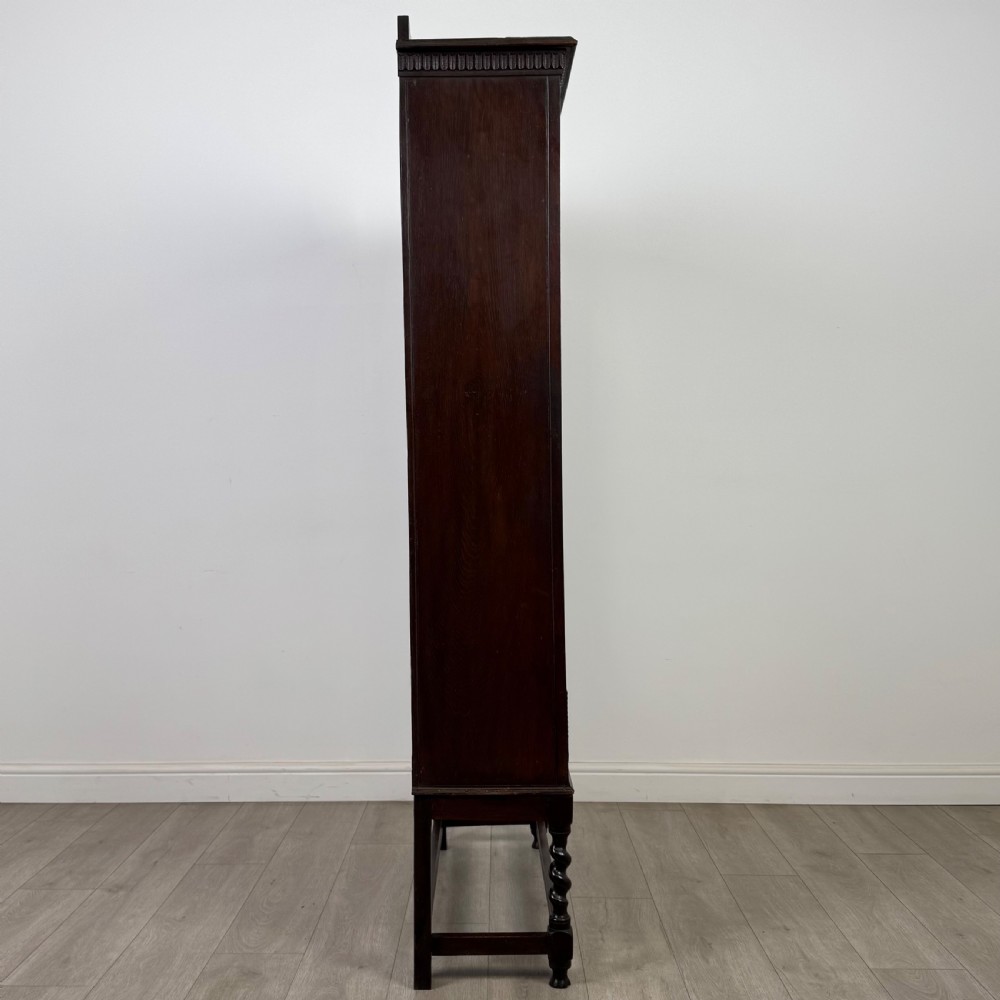 A dark oak Edwardian glazed display cabinet featuring two leaded glass doors, a lower drawer, and barley twist legs connected by stretchers. View XII