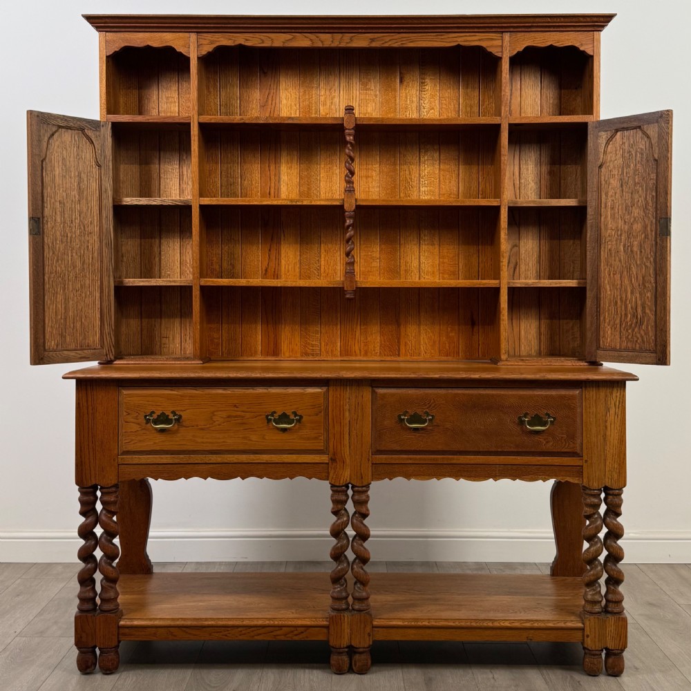A golden oak kitchen dresser featuring an upper shelving rack with side cupboards and a lower base with two drawers, barley twist legs, and an open pot board. View II