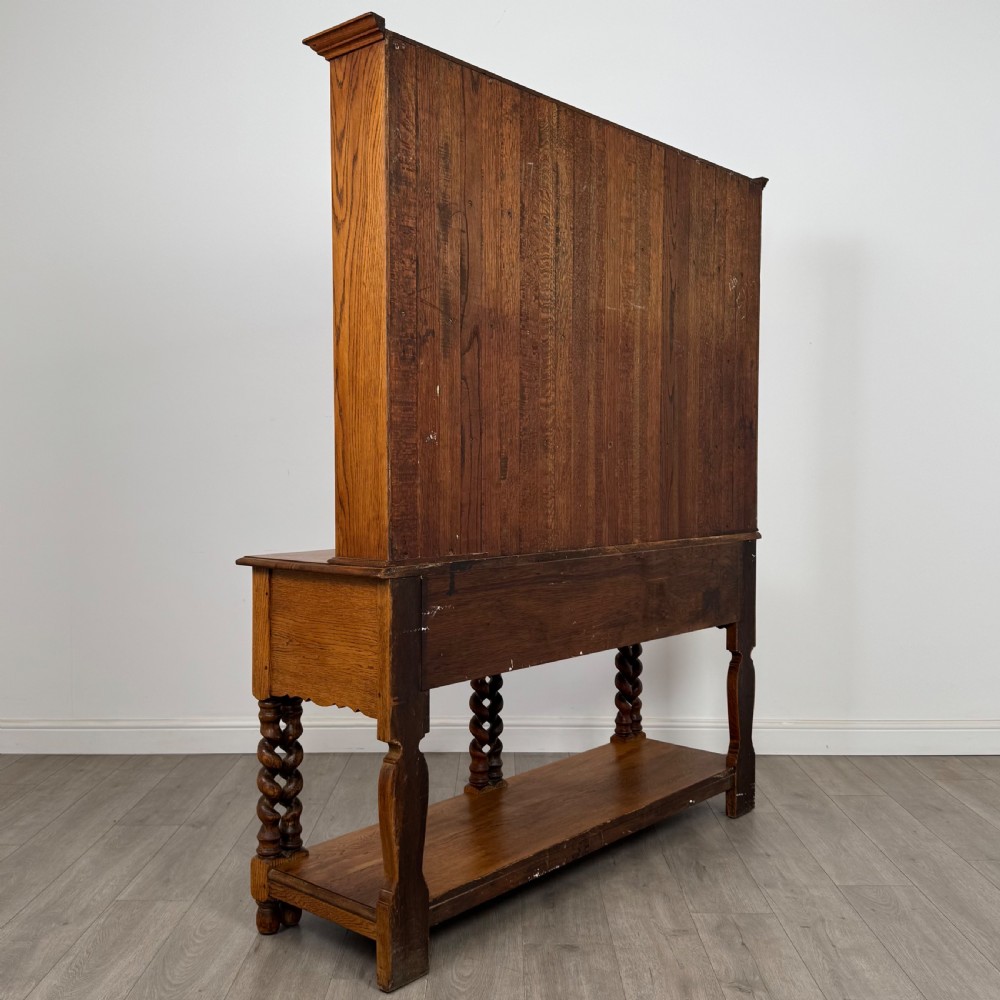 A golden oak kitchen dresser featuring an upper shelving rack with side cupboards and a lower base with two drawers, barley twist legs, and an open pot board. View V