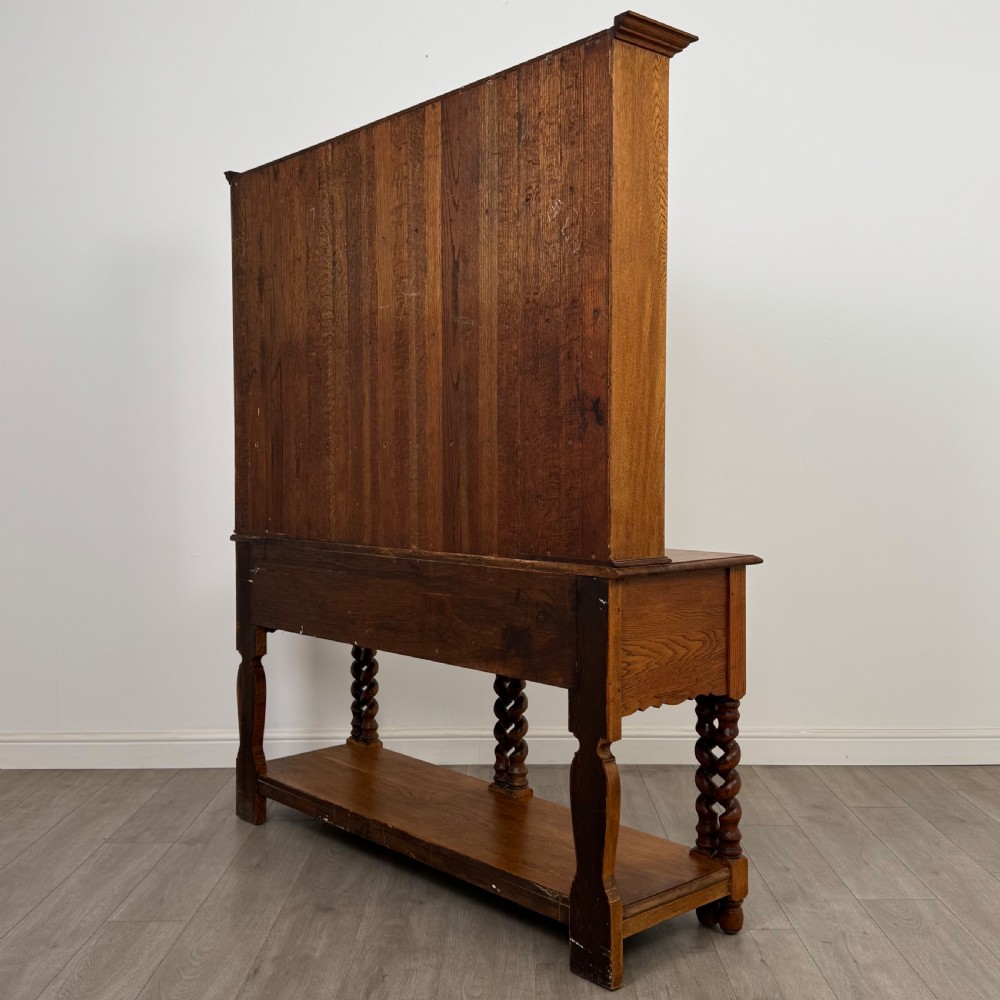 A golden oak kitchen dresser featuring an upper shelving rack with side cupboards and a lower base with two drawers, barley twist legs, and an open pot board. View VII