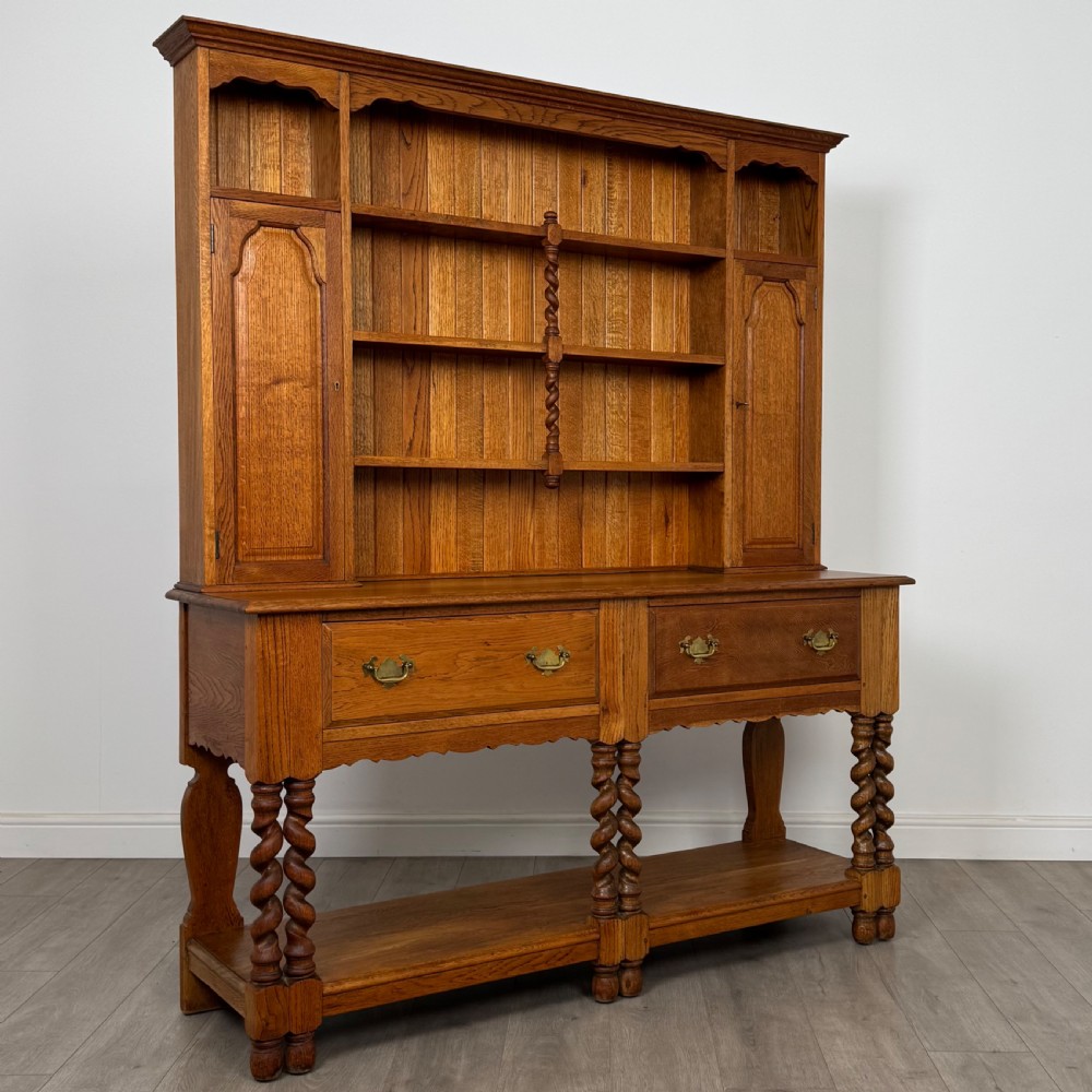 A golden oak kitchen dresser featuring an upper shelving rack with side cupboards and a lower base with two drawers, barley twist legs, and an open pot board. View IX