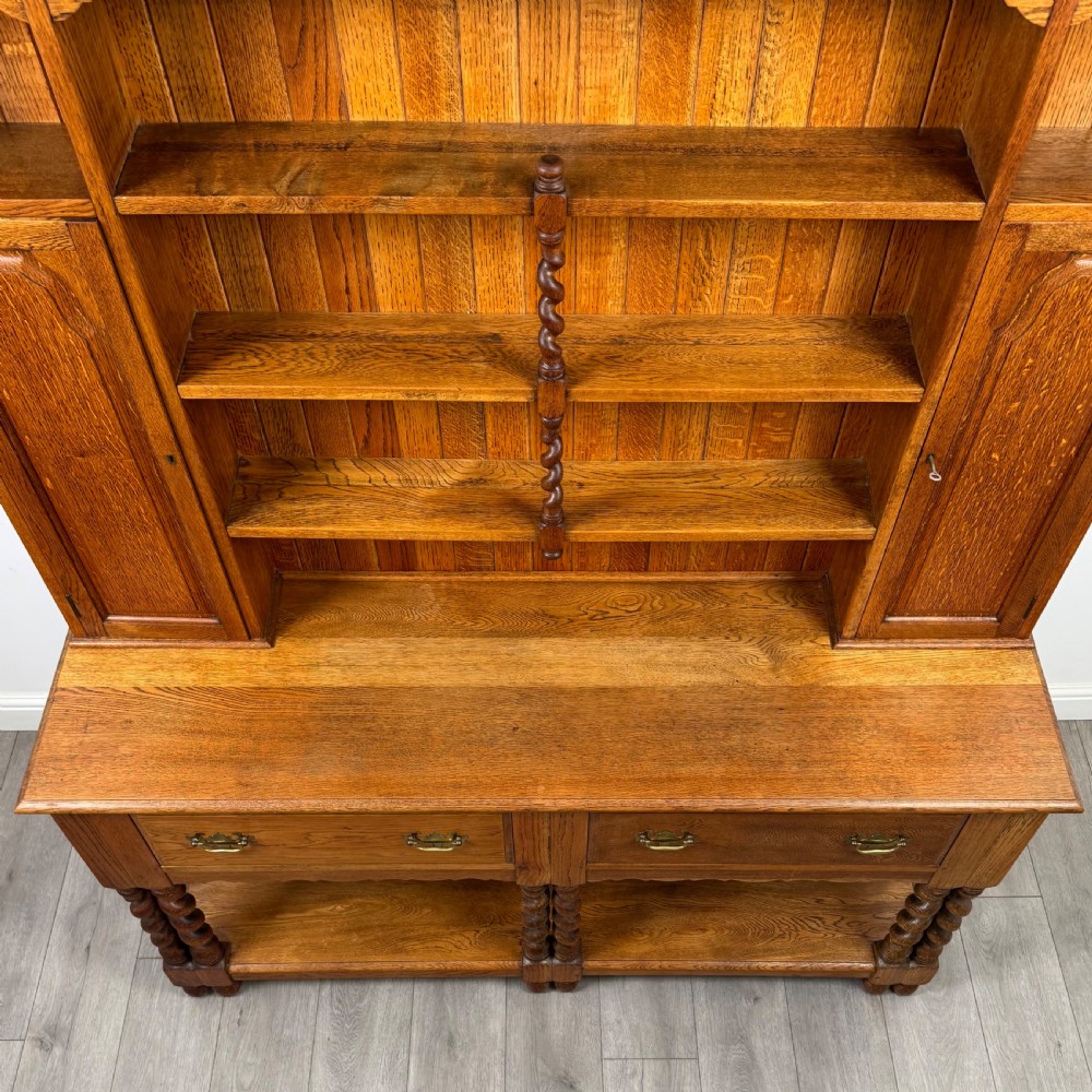 A golden oak kitchen dresser featuring an upper shelving rack with side cupboards and a lower base with two drawers, barley twist legs, and an open pot board. View X