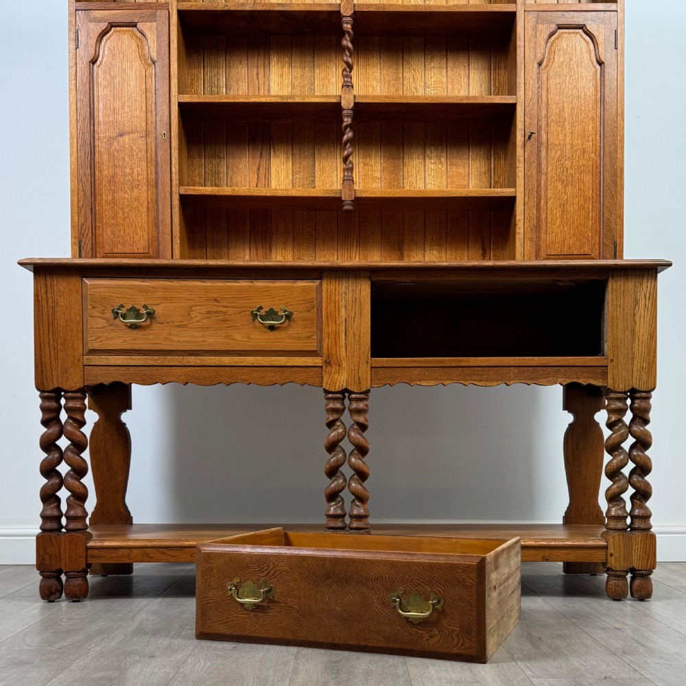 A golden oak kitchen dresser featuring an upper shelving rack with side cupboards and a lower base with two drawers, barley twist legs, and an open pot board. View XI