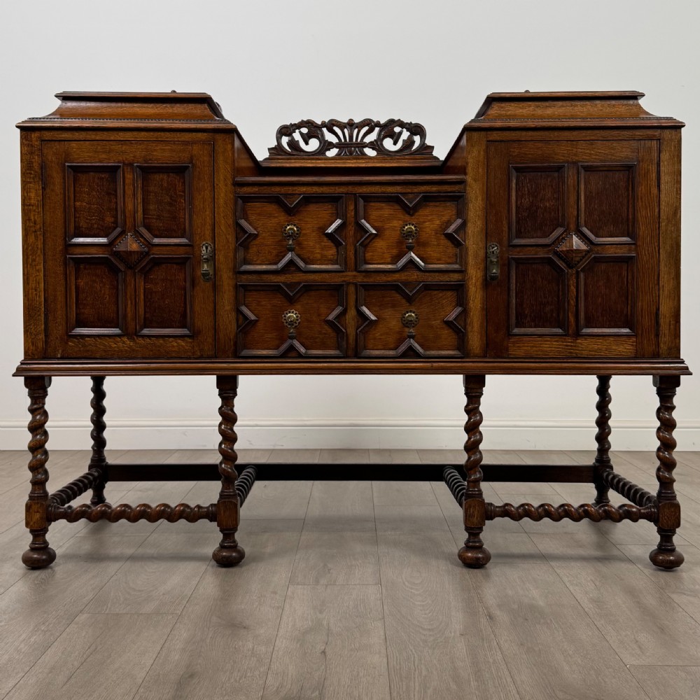 A 20th-century Jacobean style golden oak sideboard featuring geometric moulding, central drawers, cupboard doors, and barley twist legs.