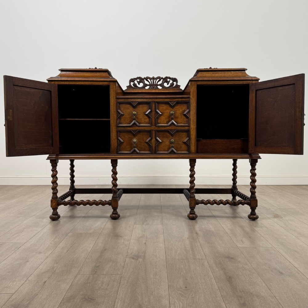 A 20th-century Jacobean style golden oak sideboard featuring geometric moulding, central drawers, cupboard doors, and barley twist legs. View II