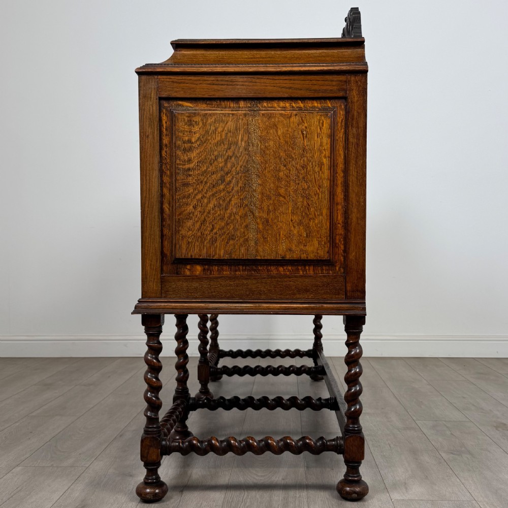 A 20th-century Jacobean style golden oak sideboard featuring geometric moulding, central drawers, cupboard doors, and barley twist legs. View IV
