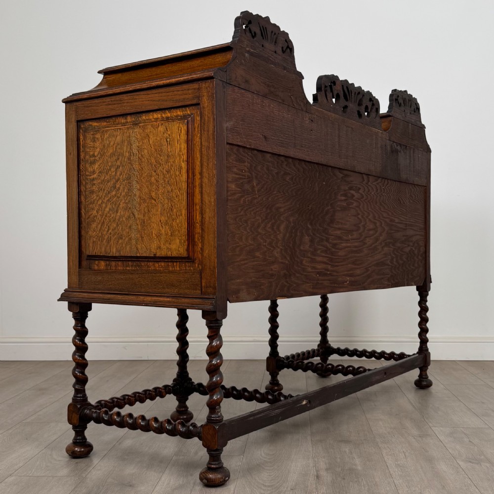 A 20th-century Jacobean style golden oak sideboard featuring geometric moulding, central drawers, cupboard doors, and barley twist legs. View V