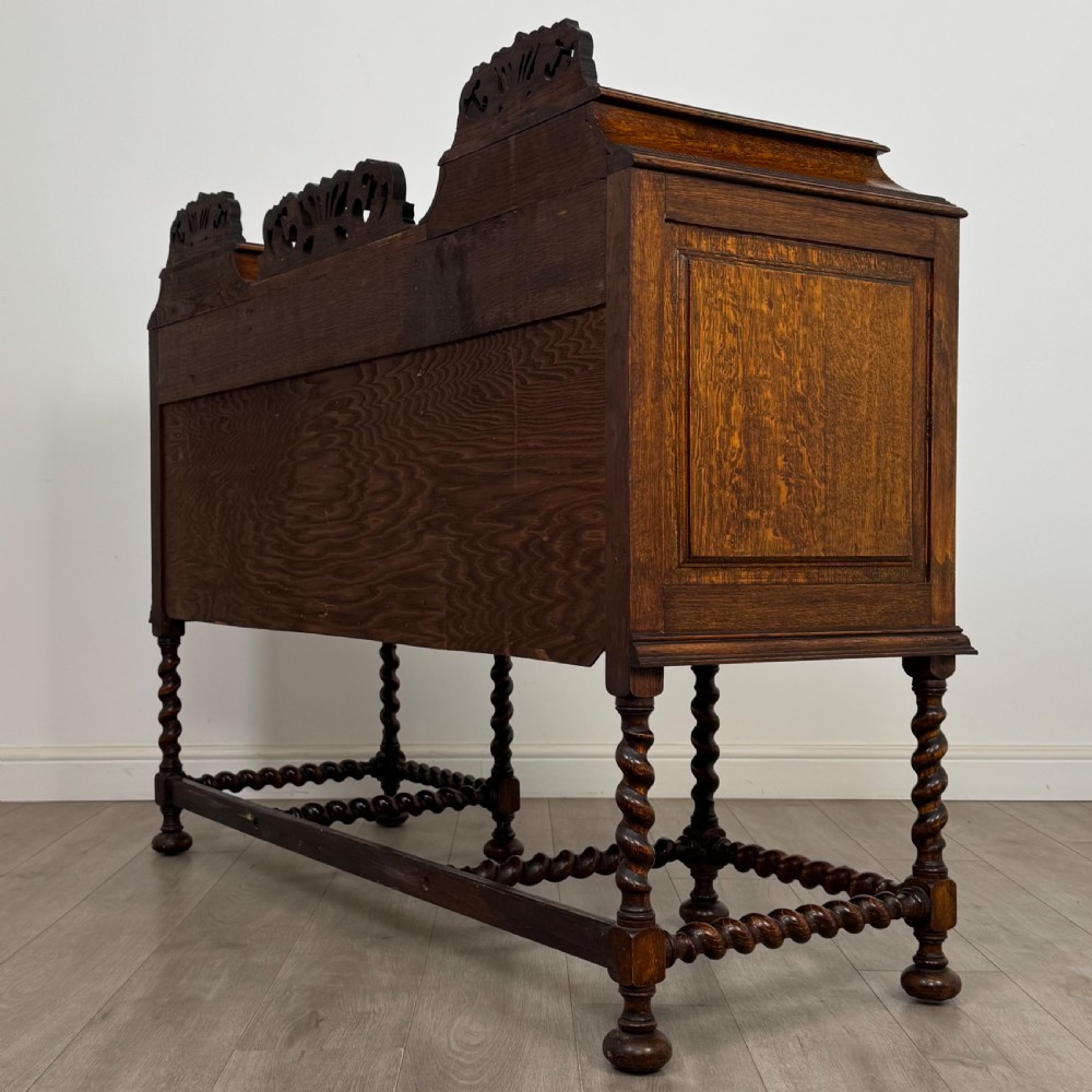 A 20th-century Jacobean style golden oak sideboard featuring geometric moulding, central drawers, cupboard doors, and barley twist legs. View VII