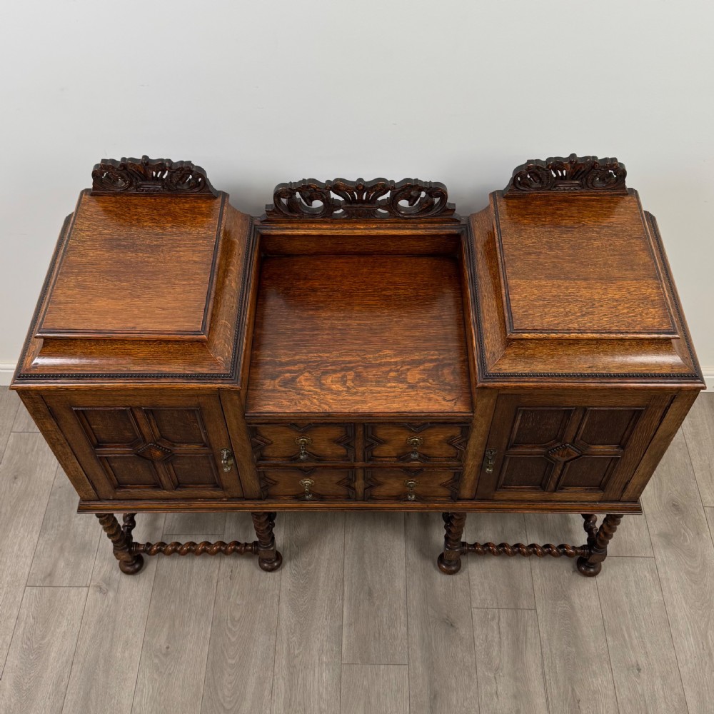 A 20th-century Jacobean style golden oak sideboard featuring geometric moulding, central drawers, cupboard doors, and barley twist legs. View X