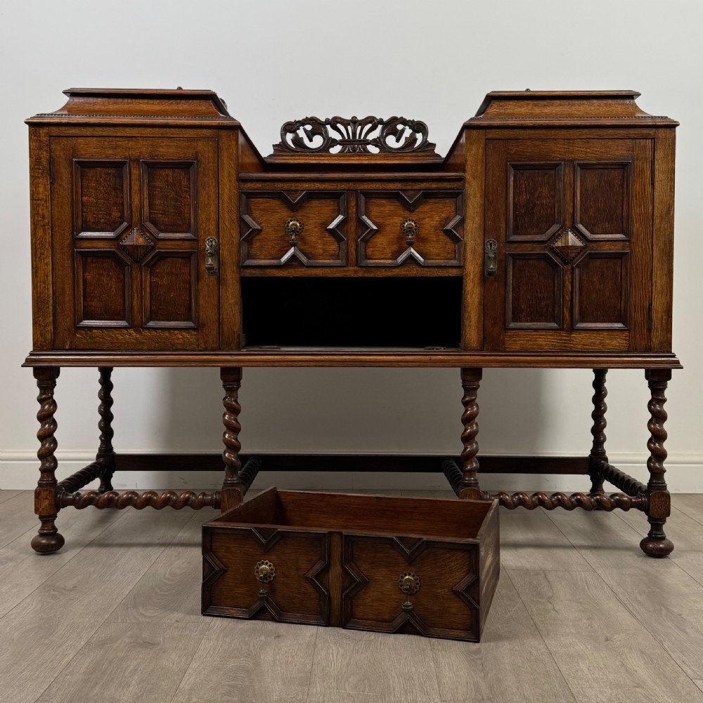 A 20th-century Jacobean style golden oak sideboard featuring geometric moulding, central drawers, cupboard doors, and barley twist legs. View XI