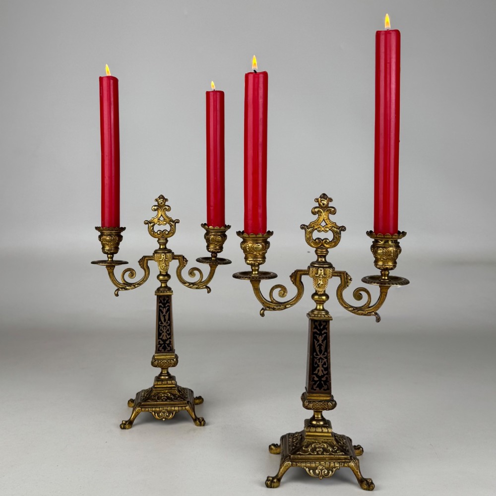 A pair of 19th-century French brass candelabra featuring ornate scrollwork arms and dark enamel inlaid details.