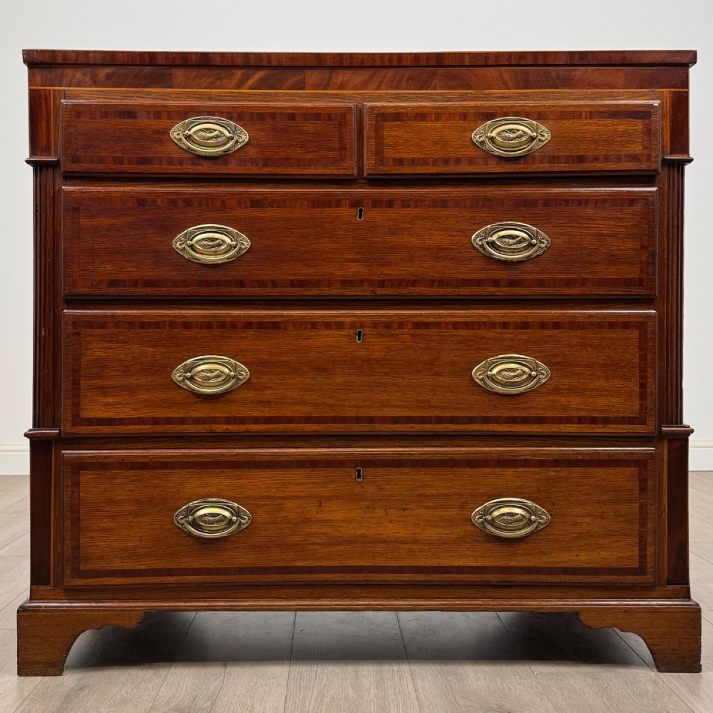 An 18th-century Georgian oak chest of drawers featuring two short drawers over three long drawers, brass handles, crossbanded inlay, reeded side columns, and bracket feet.