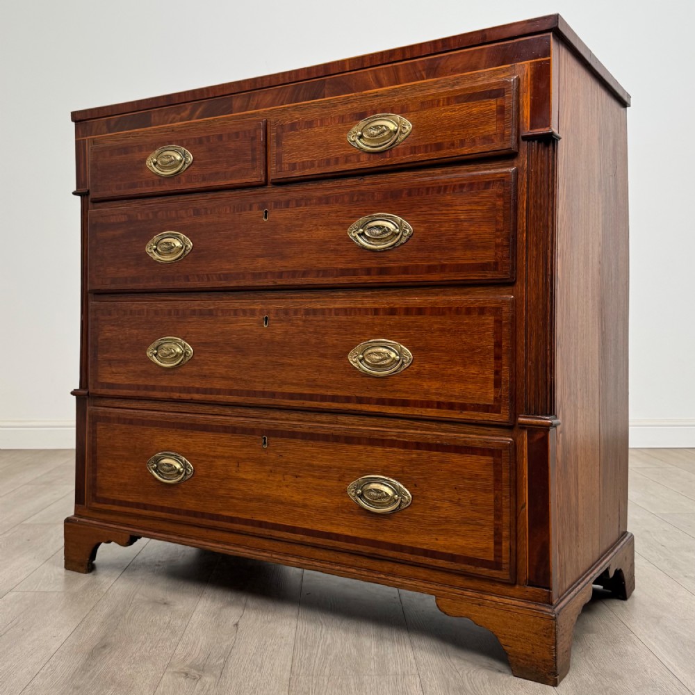 An 18th-century Georgian oak chest of drawers featuring two short drawers over three long drawers, brass handles, crossbanded inlay, reeded side columns, and bracket feet. View II