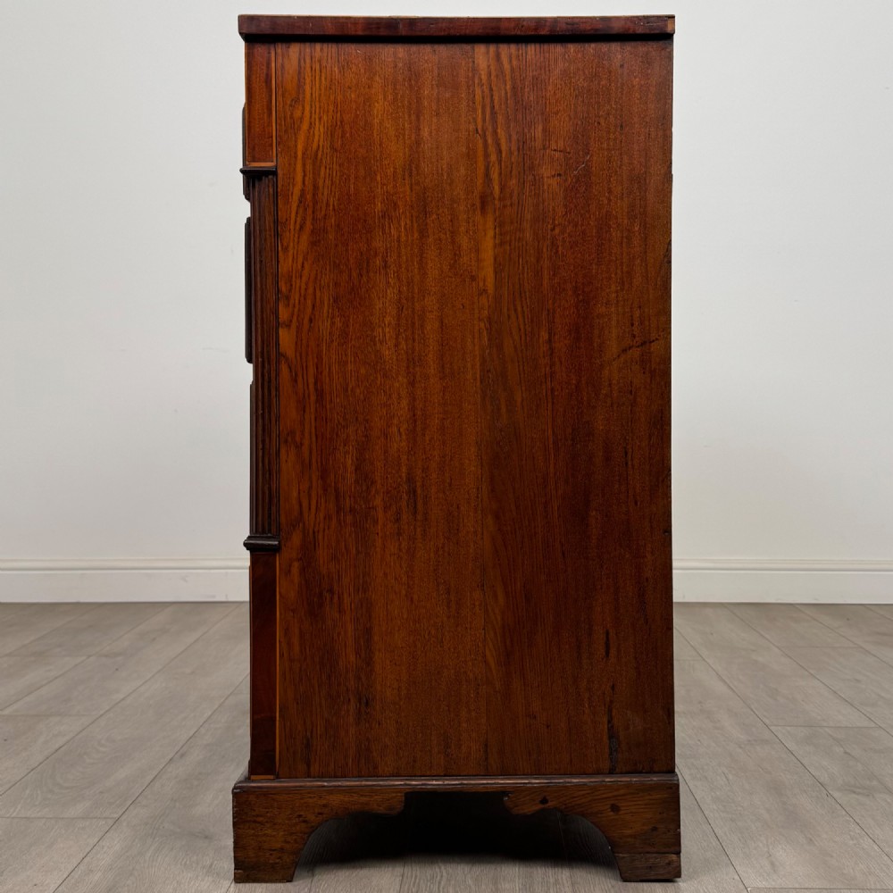 An 18th-century Georgian oak chest of drawers featuring two short drawers over three long drawers, brass handles, crossbanded inlay, reeded side columns, and bracket feet. View III