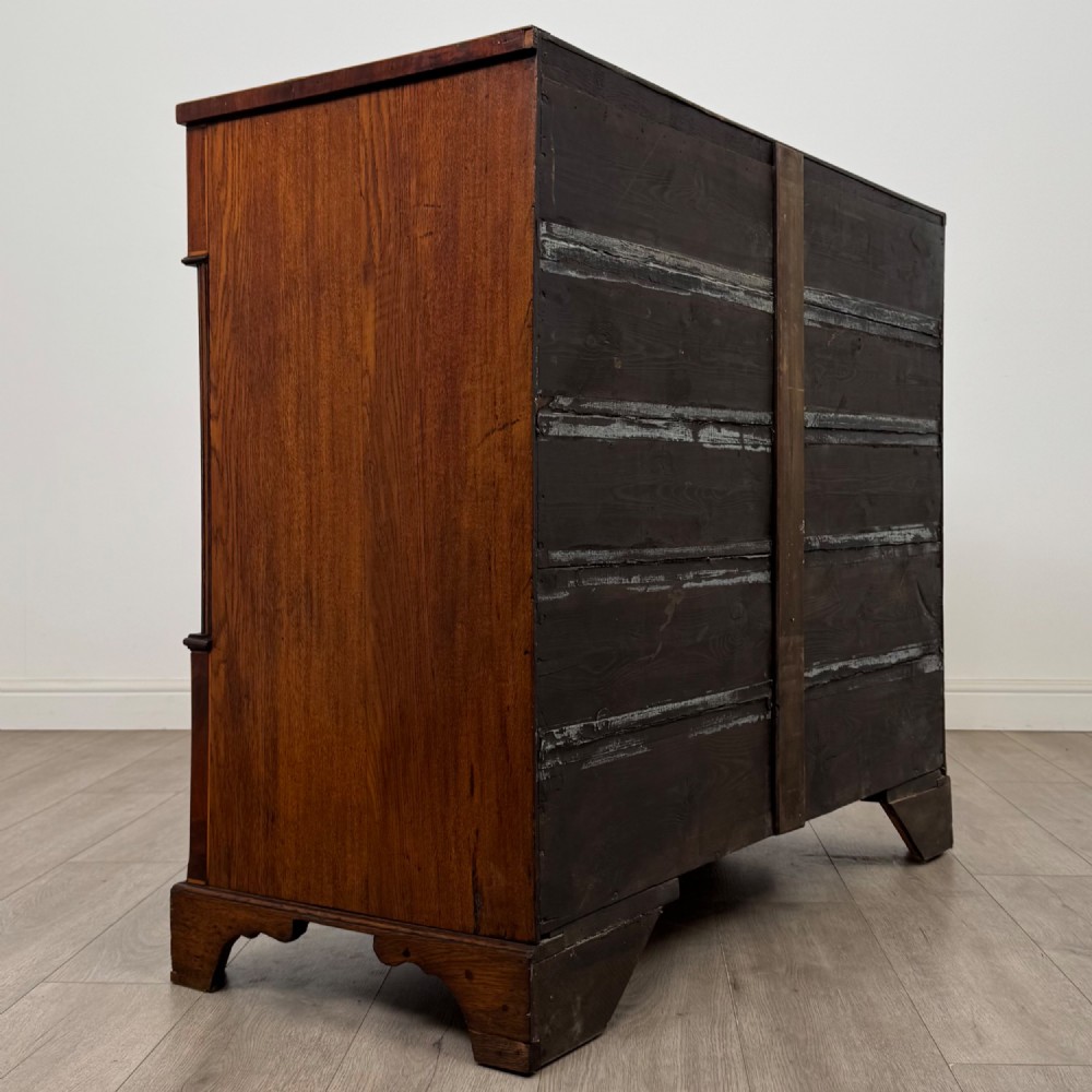 An 18th-century Georgian oak chest of drawers featuring two short drawers over three long drawers, brass handles, crossbanded inlay, reeded side columns, and bracket feet. View IV