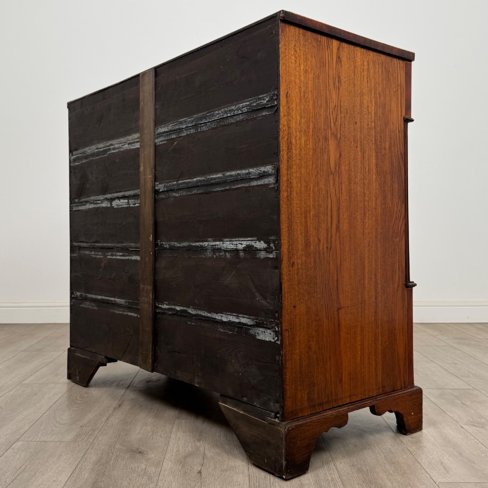An 18th-century Georgian oak chest of drawers featuring two short drawers over three long drawers, brass handles, crossbanded inlay, reeded side columns, and bracket feet. View VI