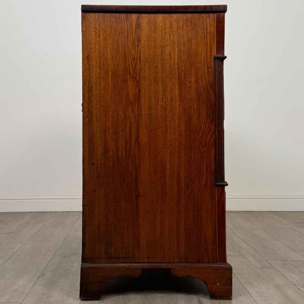 An 18th-century Georgian oak chest of drawers featuring two short drawers over three long drawers, brass handles, crossbanded inlay, reeded side columns, and bracket feet. View VII