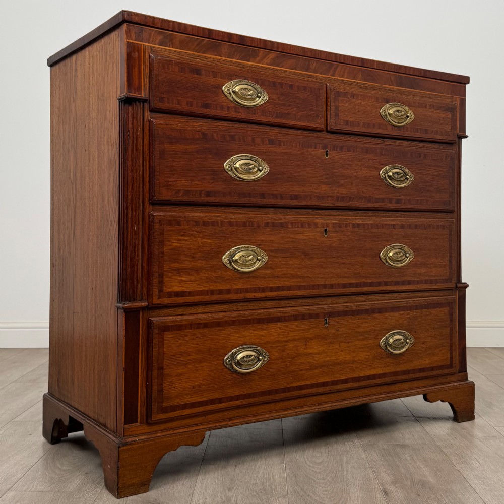 An 18th-century Georgian oak chest of drawers featuring two short drawers over three long drawers, brass handles, crossbanded inlay, reeded side columns, and bracket feet. View VIII