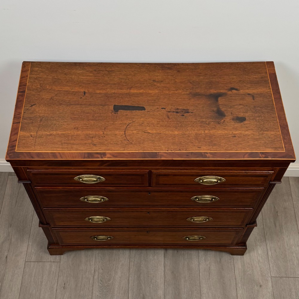 An 18th-century Georgian oak chest of drawers featuring two short drawers over three long drawers, brass handles, crossbanded inlay, reeded side columns, and bracket feet. View IX
