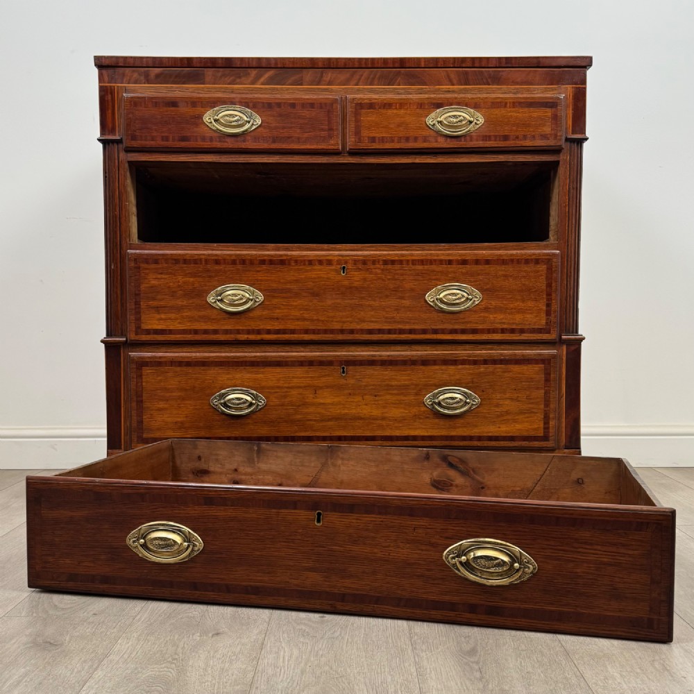 An 18th-century Georgian oak chest of drawers featuring two short drawers over three long drawers, brass handles, crossbanded inlay, reeded side columns, and bracket feet. View X