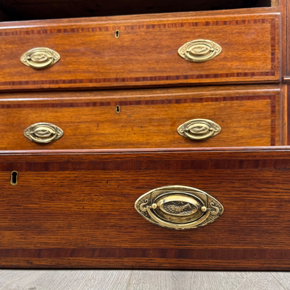 An 18th-century Georgian oak chest of drawers featuring two short drawers over three long drawers, brass handles, crossbanded inlay, reeded side columns, and bracket feet. View XI