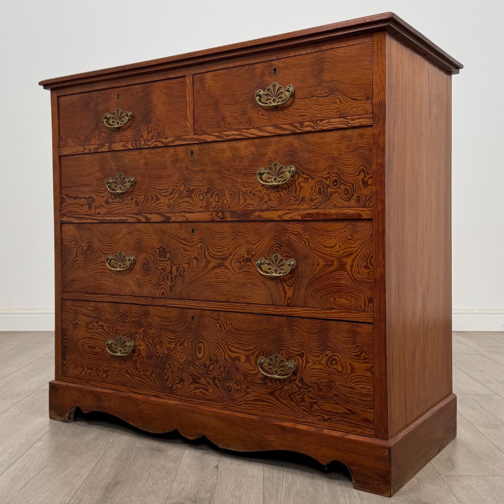 A Victorian nineteenth-century pitch pine chest of drawers featuring a prominent figured wood grain, brass drop handles, a two-over-three drawer configuration, and a shaped apron base. View II