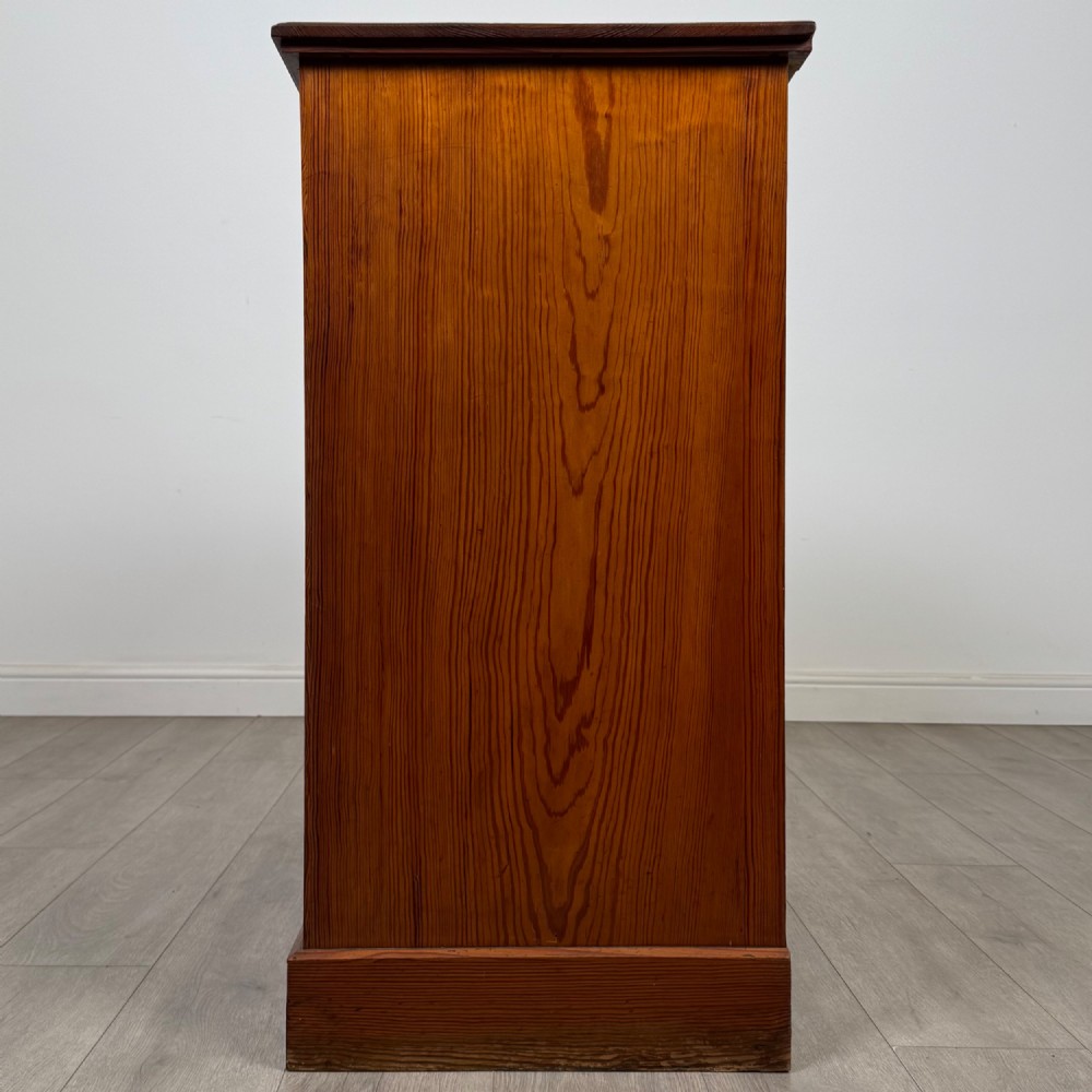 A Victorian nineteenth-century pitch pine chest of drawers featuring a prominent figured wood grain, brass drop handles, a two-over-three drawer configuration, and a shaped apron base. View III