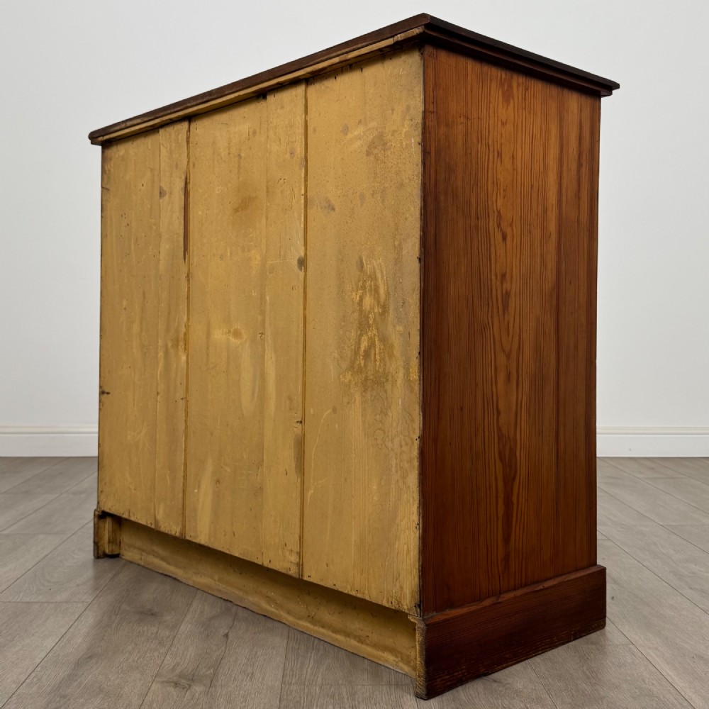 A Victorian nineteenth-century pitch pine chest of drawers featuring a prominent figured wood grain, brass drop handles, a two-over-three drawer configuration, and a shaped apron base. View VI