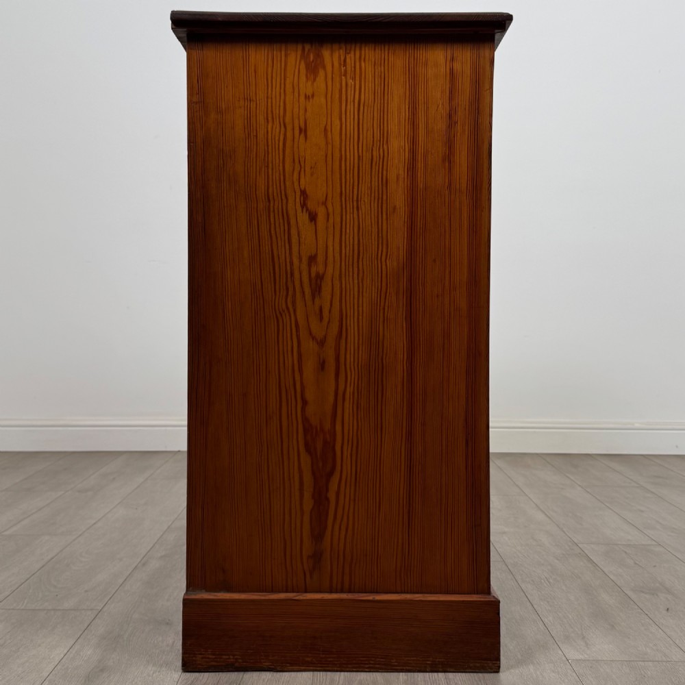 A Victorian nineteenth-century pitch pine chest of drawers featuring a prominent figured wood grain, brass drop handles, a two-over-three drawer configuration, and a shaped apron base. View VII