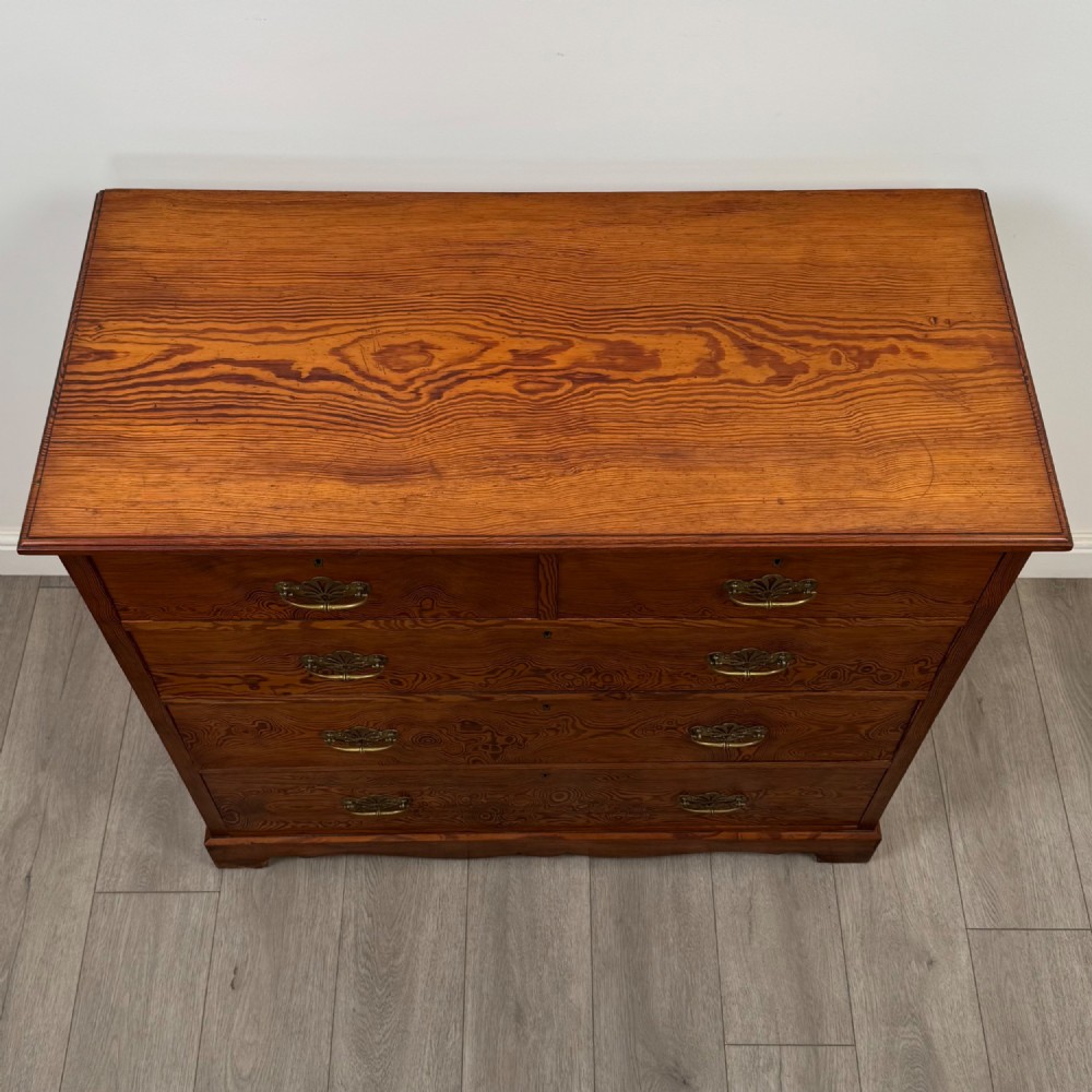 A Victorian nineteenth-century pitch pine chest of drawers featuring a prominent figured wood grain, brass drop handles, a two-over-three drawer configuration, and a shaped apron base. View IX