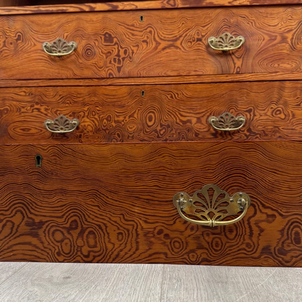 A Victorian nineteenth-century pitch pine chest of drawers featuring a prominent figured wood grain, brass drop handles, a two-over-three drawer configuration, and a shaped apron base. View XI