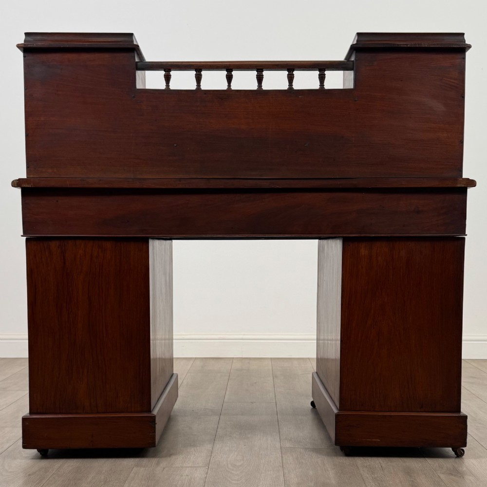 A 19th-century Victorian mahogany Dickens desk featuring a twin-pedestal design, raised superstructure with drawers and spindle gallery, slant writing surface, turned timber knobs, and plinth bases. View VI