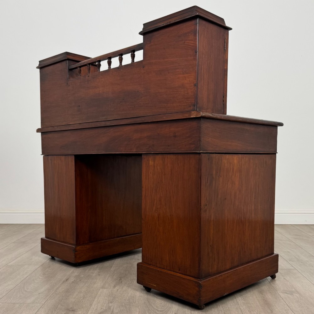 A 19th-century Victorian mahogany Dickens desk featuring a twin-pedestal design, raised superstructure with drawers and spindle gallery, slant writing surface, turned timber knobs, and plinth bases. View VII