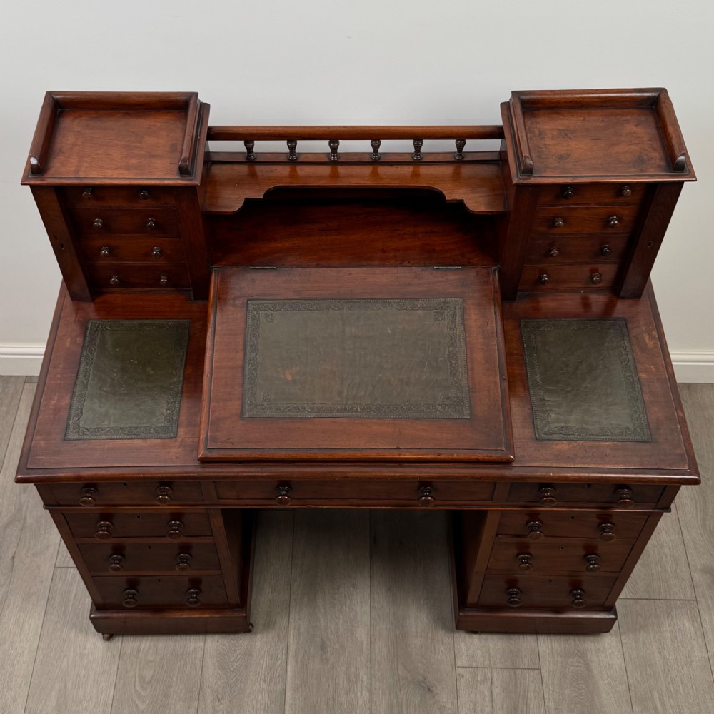 A 19th-century Victorian mahogany Dickens desk featuring a twin-pedestal design, raised superstructure with drawers and spindle gallery, slant writing surface, turned timber knobs, and plinth bases. View X
