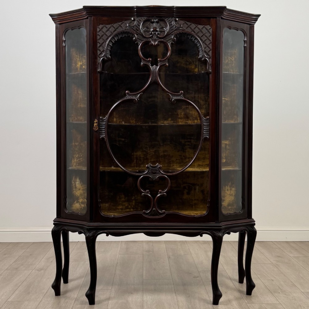 A dark mahogany display cabinet featuring glazed panels, detailed carved fretwork on the central door, and cabriole legs.