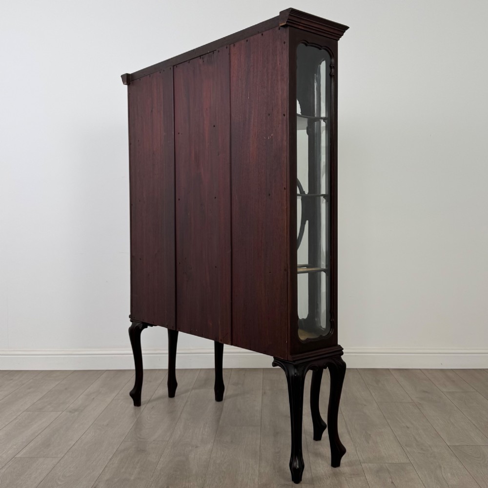 A dark mahogany display cabinet featuring glazed panels, detailed carved fretwork on the central door, and cabriole legs. View VII