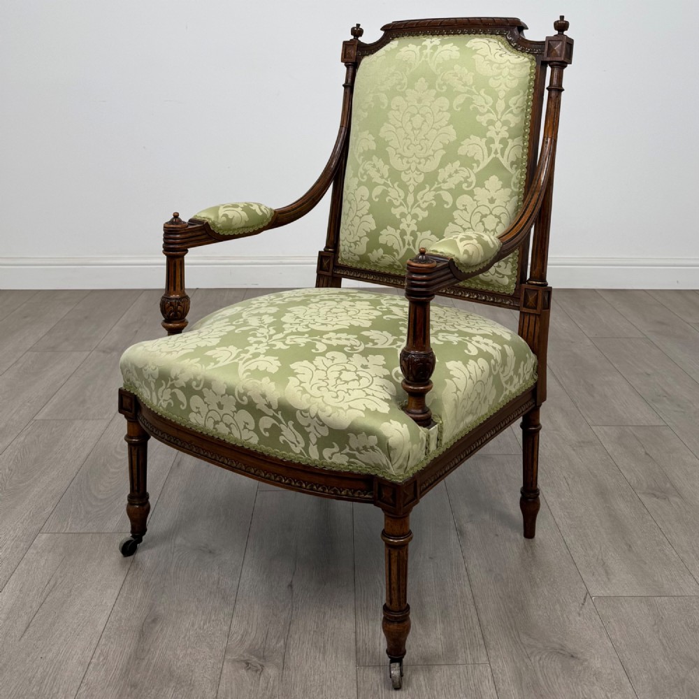 A 19th-century French open armchair featuring a carved walnut frame, fluted legs on brass castors, and green floral damask upholstery.