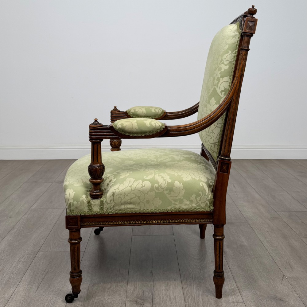 A 19th-century French open armchair featuring a carved walnut frame, fluted legs on brass castors, and green floral damask upholstery. View II