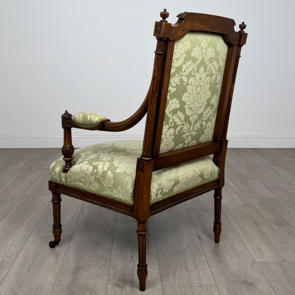 A 19th-century French open armchair featuring a carved walnut frame, fluted legs on brass castors, and green floral damask upholstery. View III