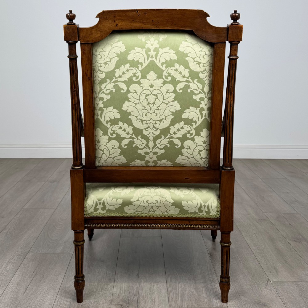 A 19th-century French open armchair featuring a carved walnut frame, fluted legs on brass castors, and green floral damask upholstery. View IV