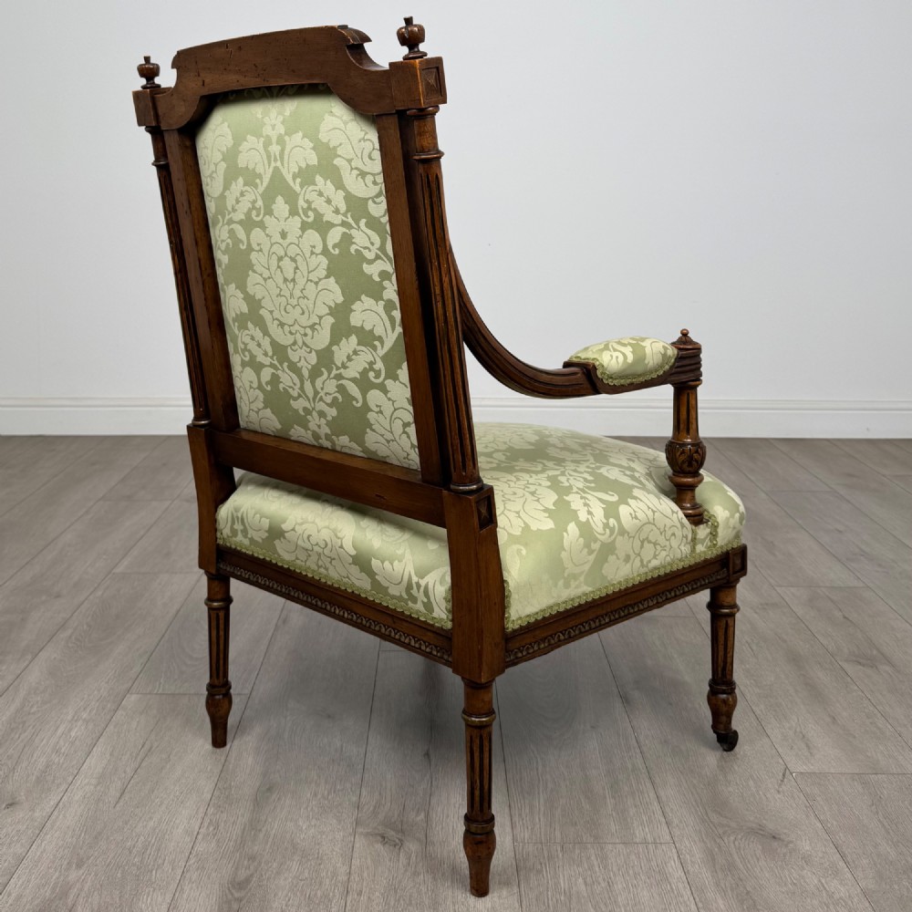A 19th-century French open armchair featuring a carved walnut frame, fluted legs on brass castors, and green floral damask upholstery. View V