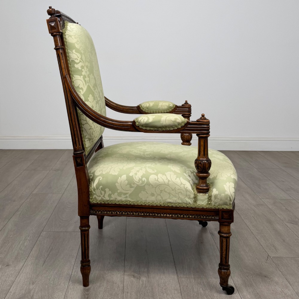 A 19th-century French open armchair featuring a carved walnut frame, fluted legs on brass castors, and green floral damask upholstery. View VI