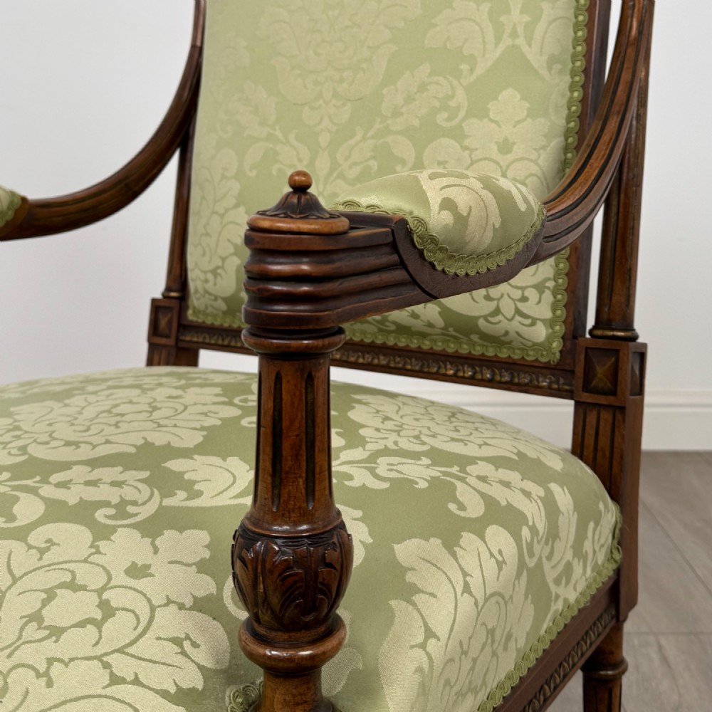 A 19th-century French open armchair featuring a carved walnut frame, fluted legs on brass castors, and green floral damask upholstery. View X