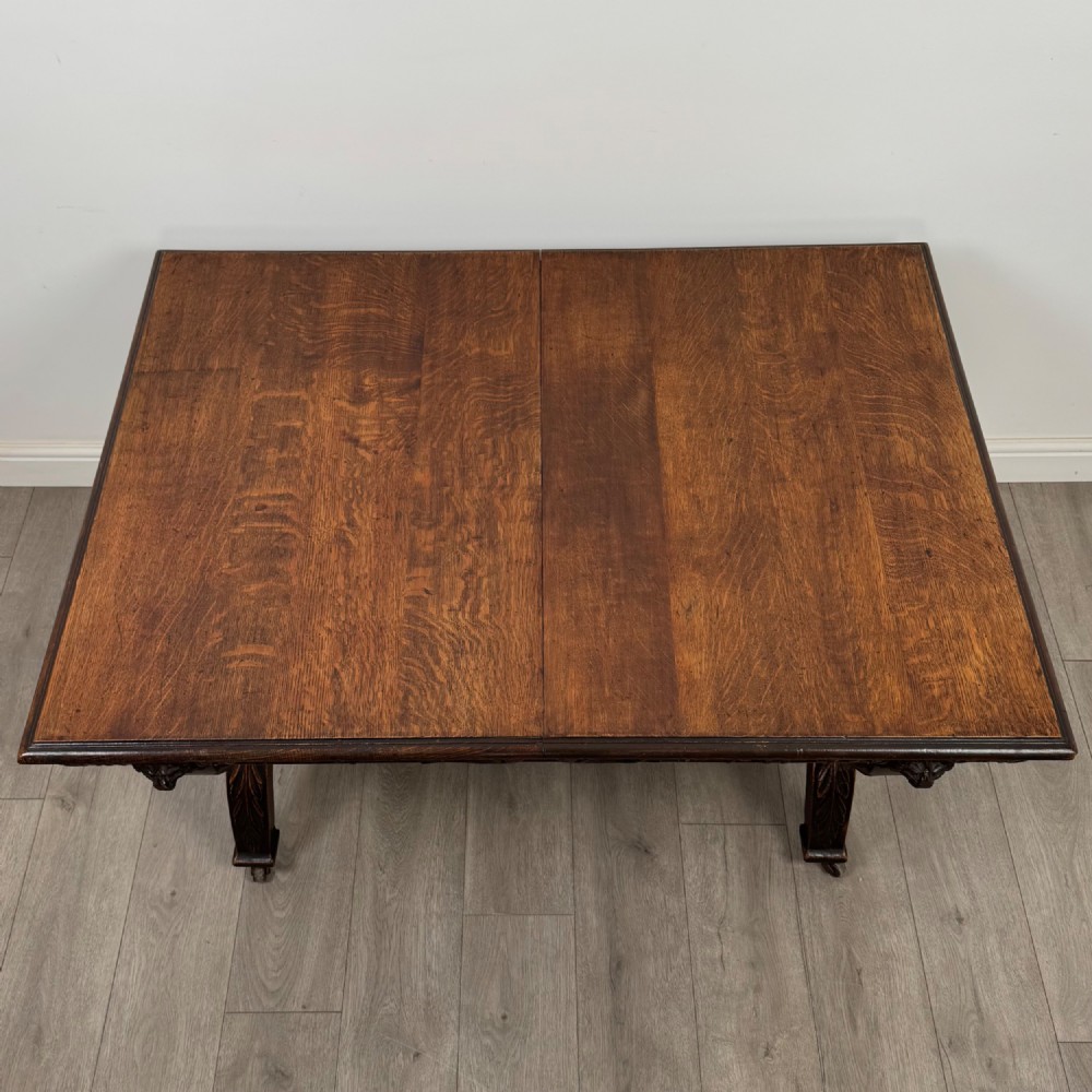A 19th-century dark carved oak centre table featuring an X-frame curule base, carved frieze, turned stretcher, and metal castors. View VI
